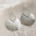 Close-up of sterling silver pear-shaped hammered dangle earrings with French hook ear wires on a marble surface.

